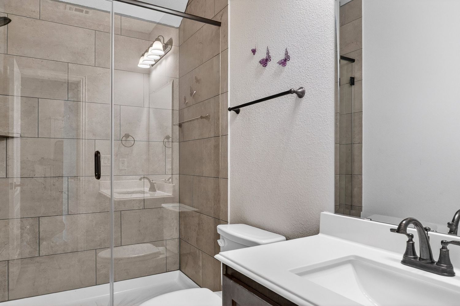Beige tiled bathroom with glass shower enclosure and modern fixtures.
