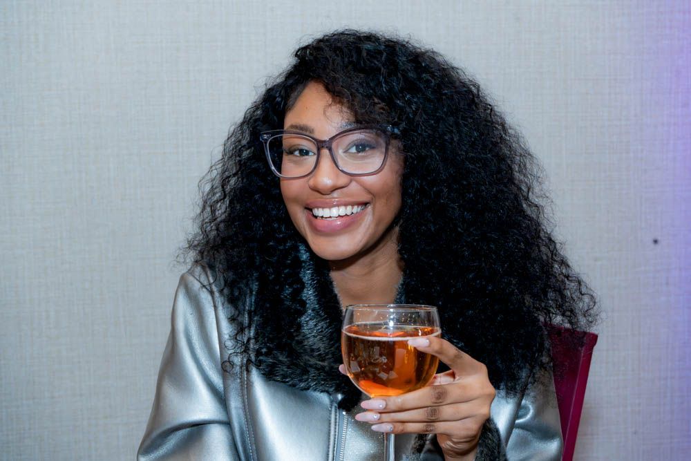 Person with curly hair enjoying a beverage in front of a grey background.