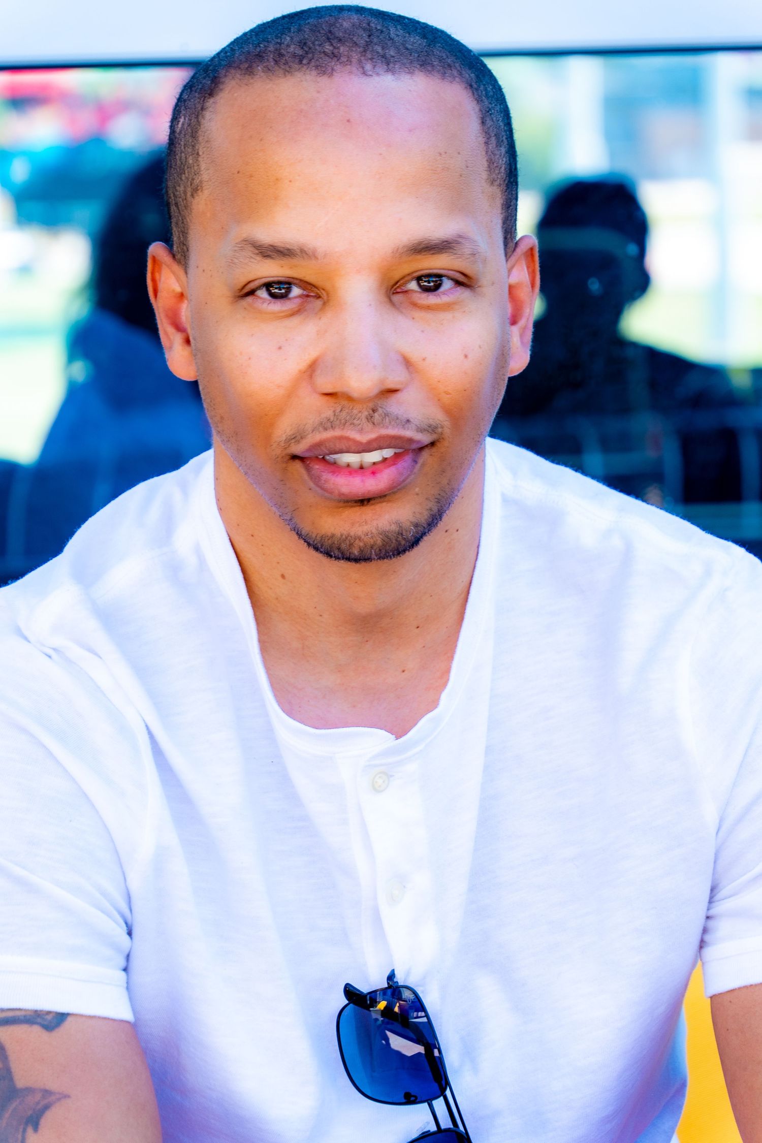 Man in white t-shirt smiling at camera in outdoor setting.