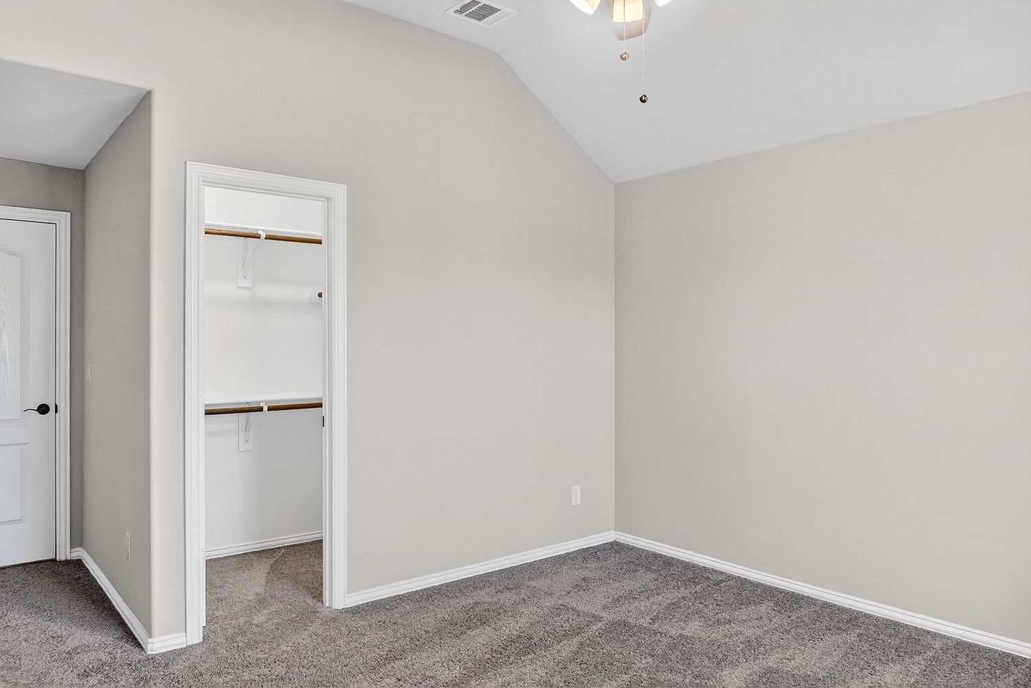 Spacious bedroom with vaulted ceiling, neutral walls, and plush carpet flooring.