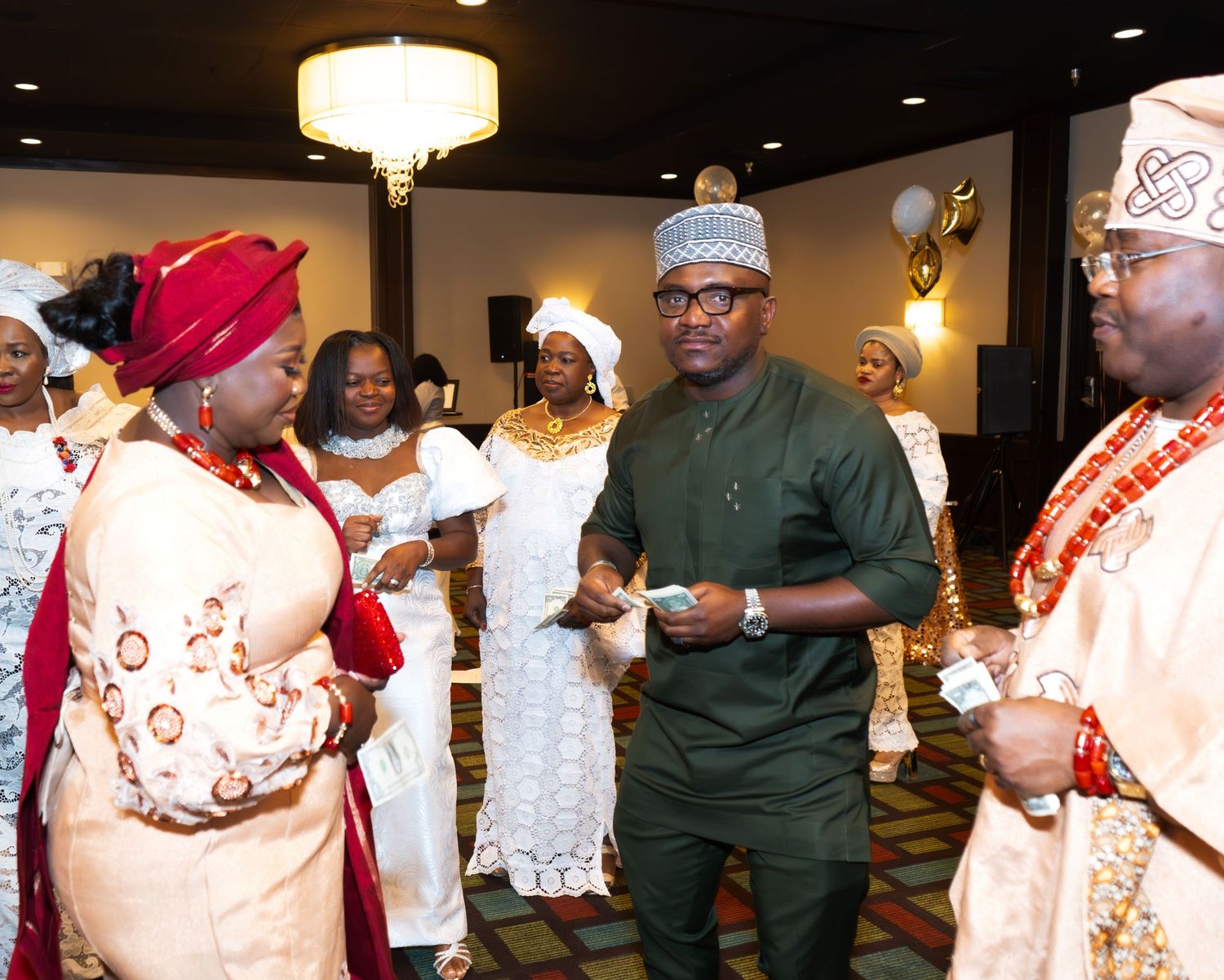 Traditional African celebration with attendees wearing cultural formal wear and headpieces in an event hall.