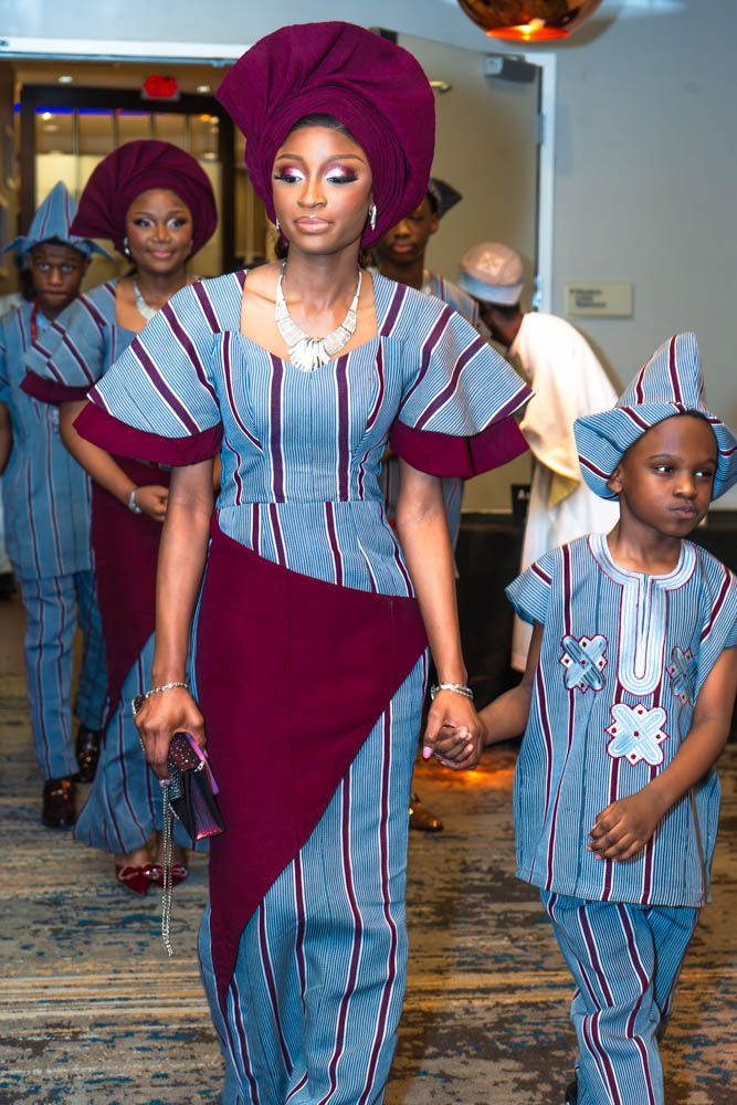 Wedding party members wearing matching blue striped and burgundy traditional African outfits walk in procession.