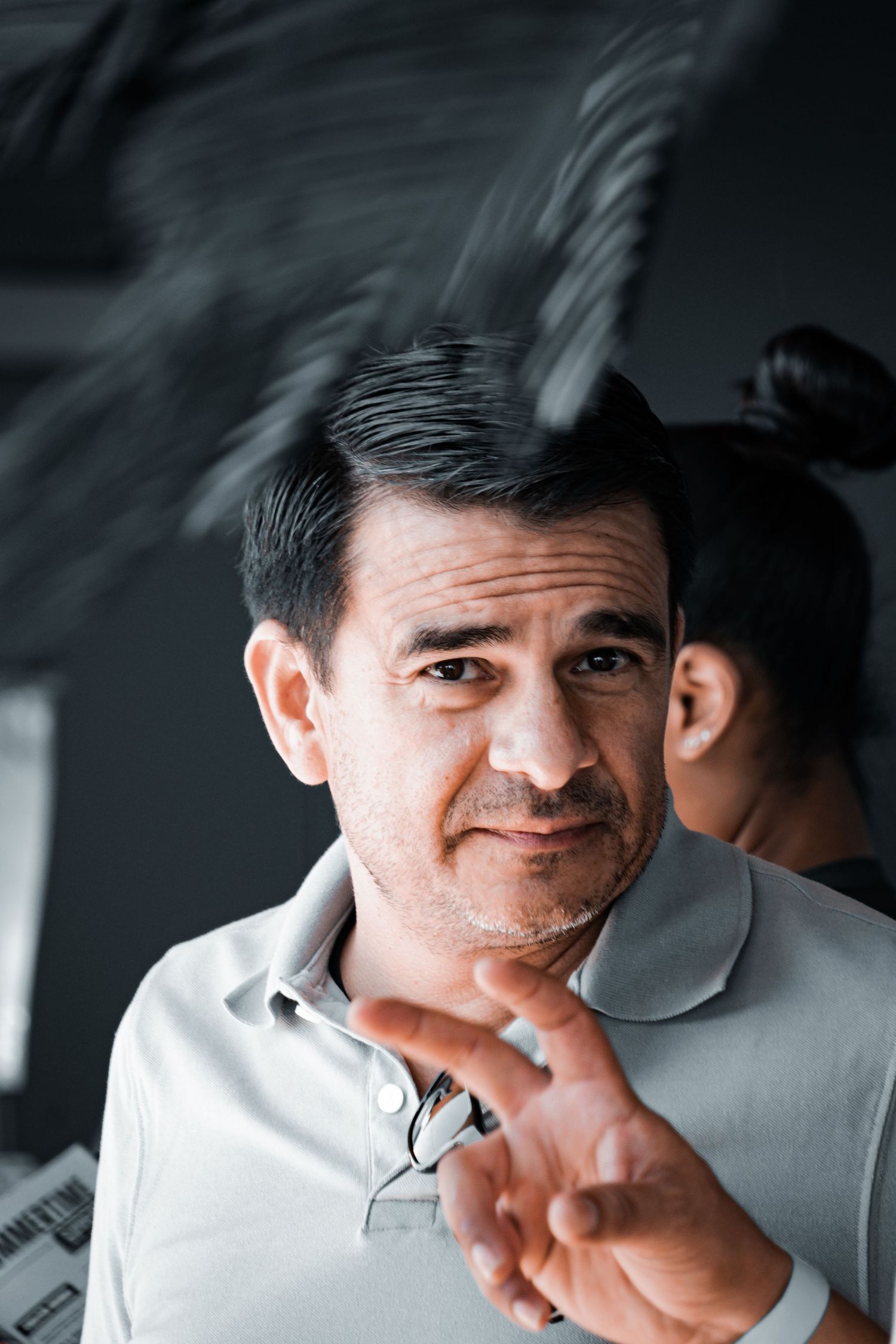 Man in grey polo shirt gesturing against dark background.