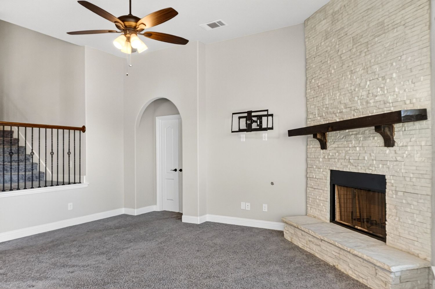 Spacious living room with stone accent wall, ceiling fan, and carpeted flooring.