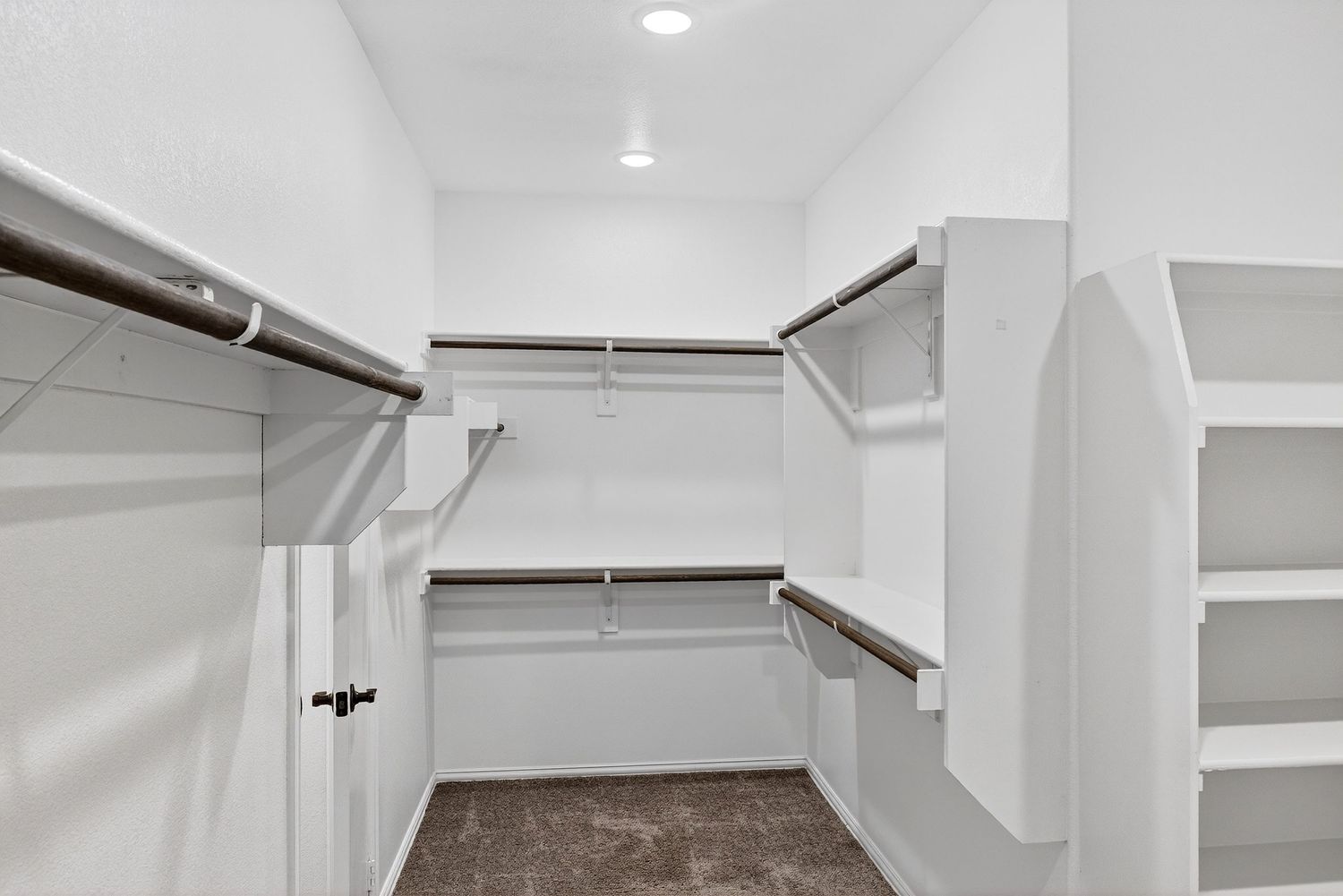 Walk-in closet with white walls, built-in shelving, and multiple clothing rods.