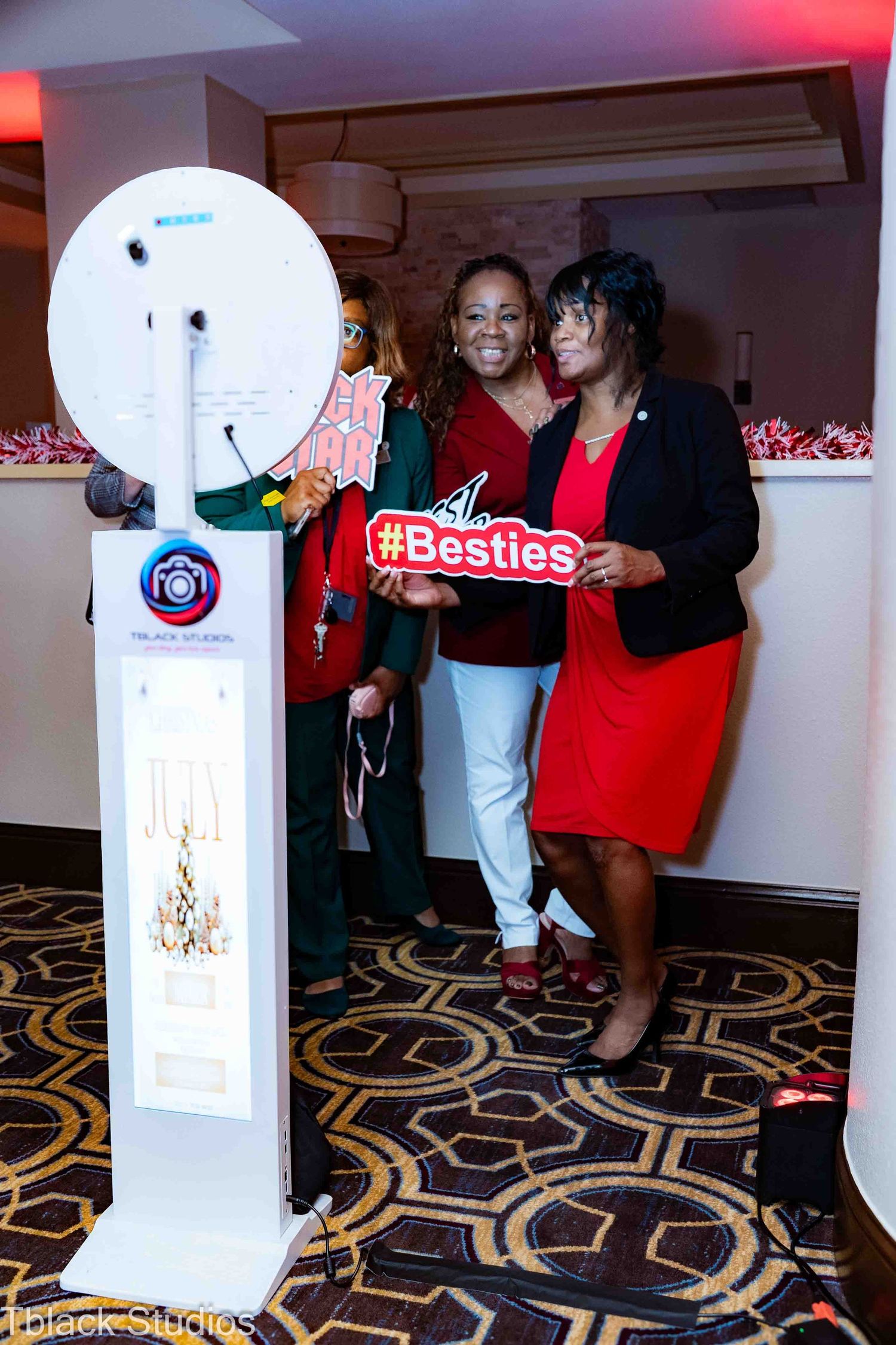 Photo booth setup in hotel hallway with decorative carpet and interactive display screen.
