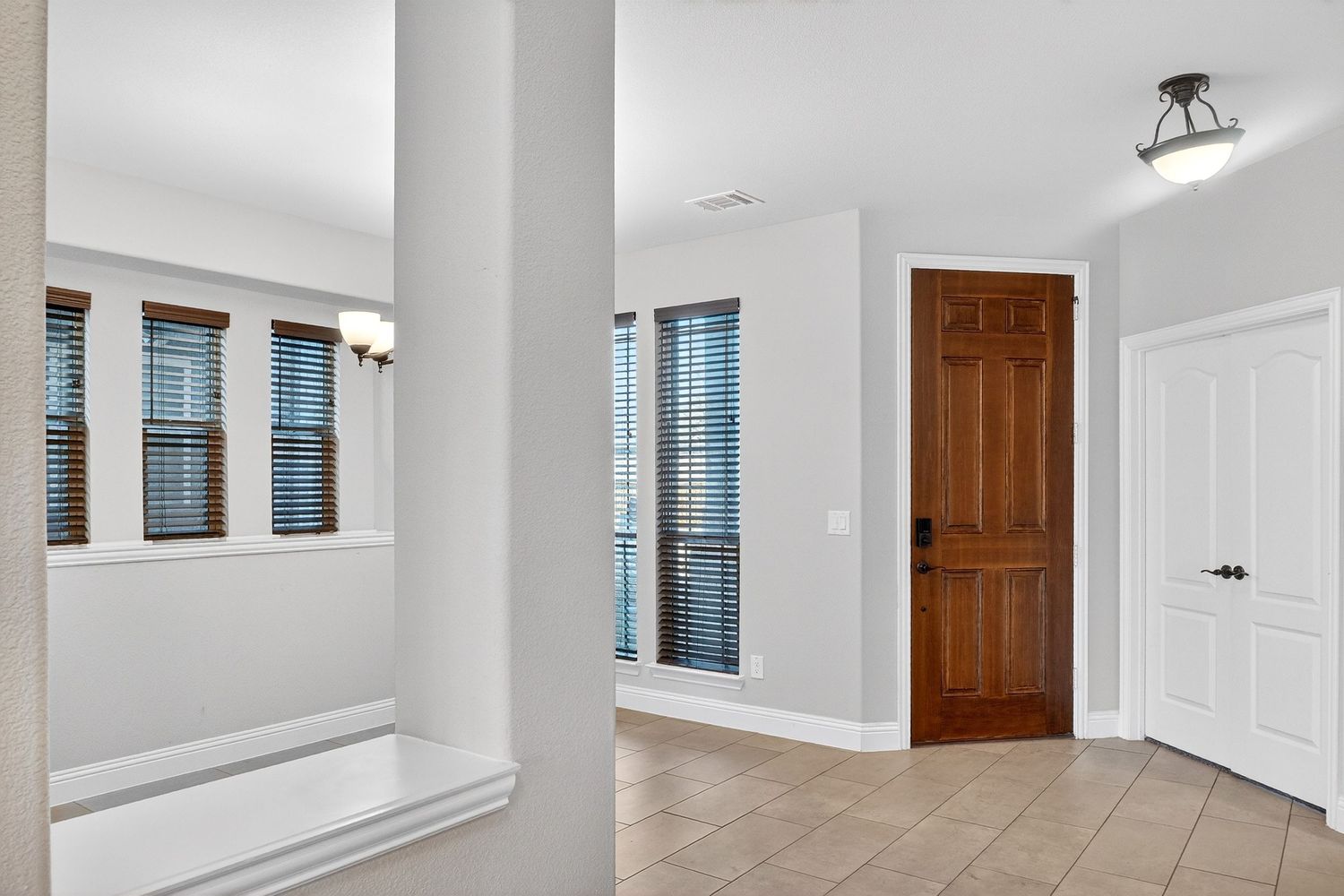 Interior room with tall windows, white trim, and wood door featuring tile flooring and column detail.