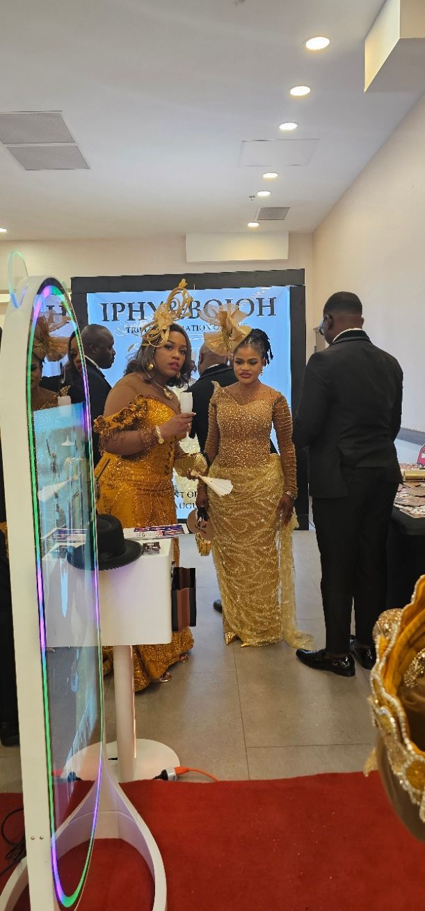People in formal attire and gold dresses gather at an event with red carpet and recessed lighting in a modern hallway.