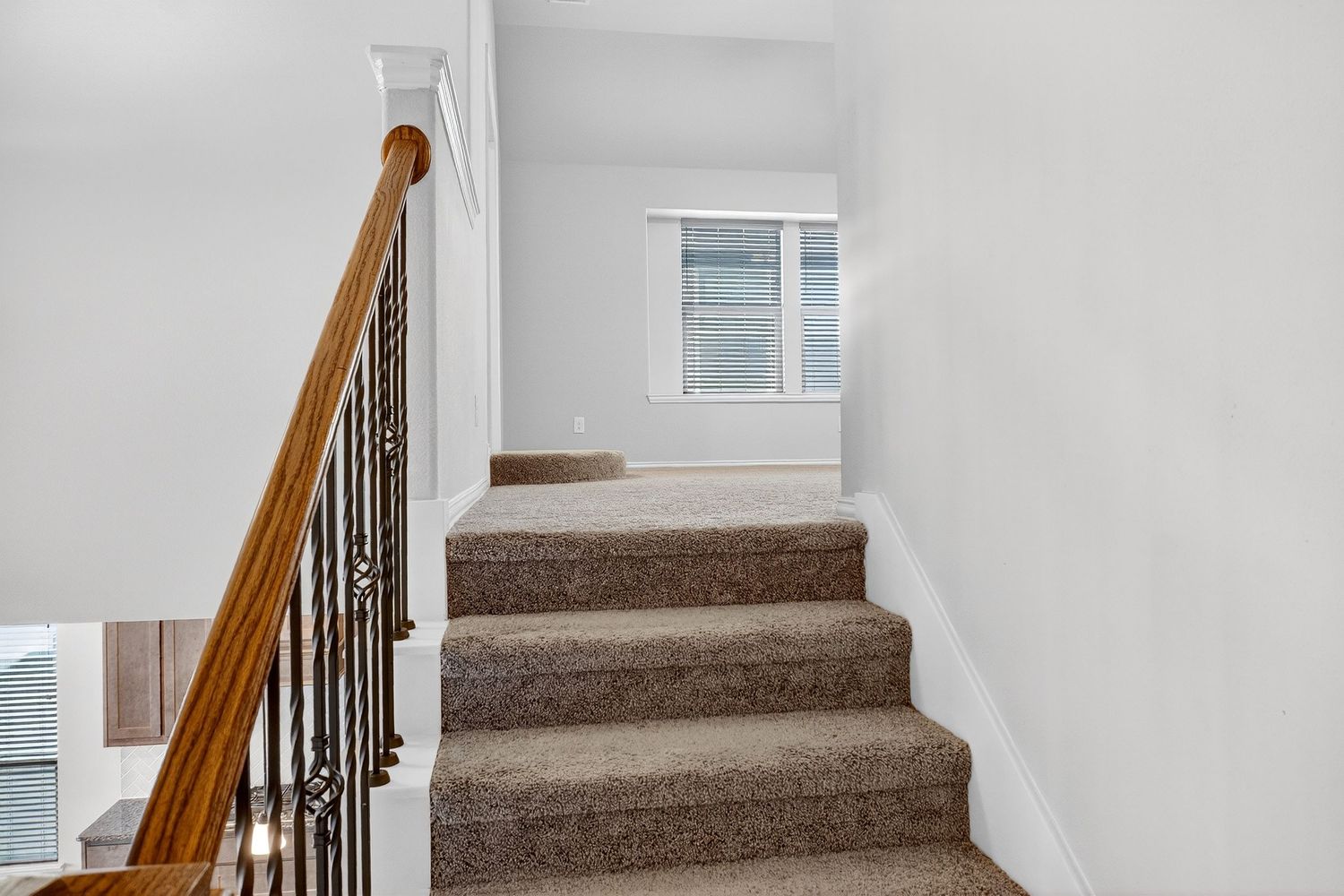 Carpeted staircase with wooden handrail and black metal balusters leading upstairs.