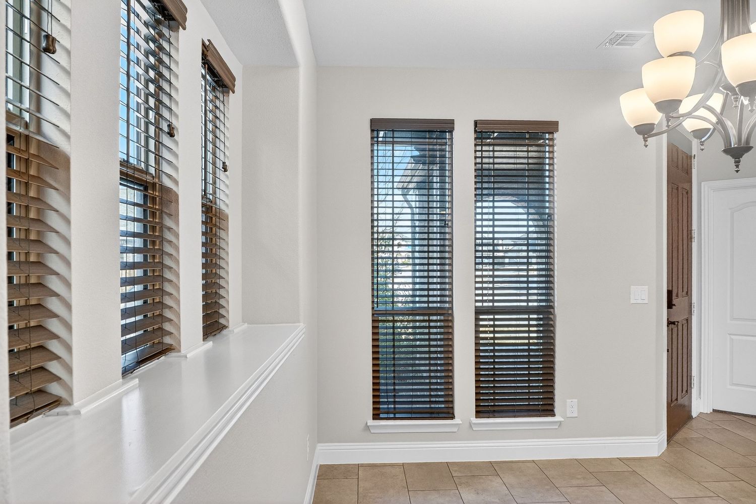 Modern home interior with high ceilings, white walls, and large windows featuring elegant pendant lighting fixtures.