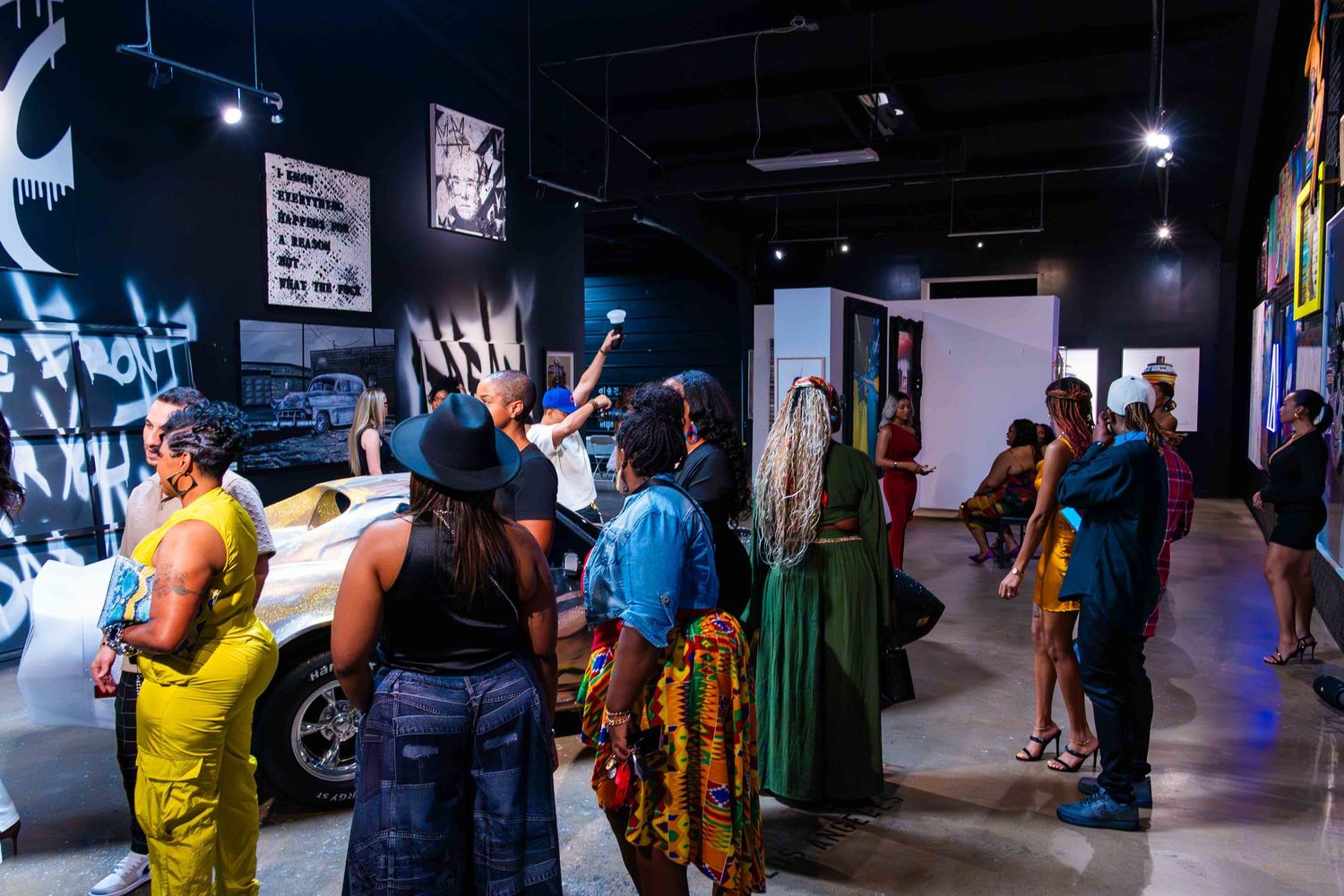 Crowd of people gathered in a dimly lit indoor space with colorful lighting and wall decorations.