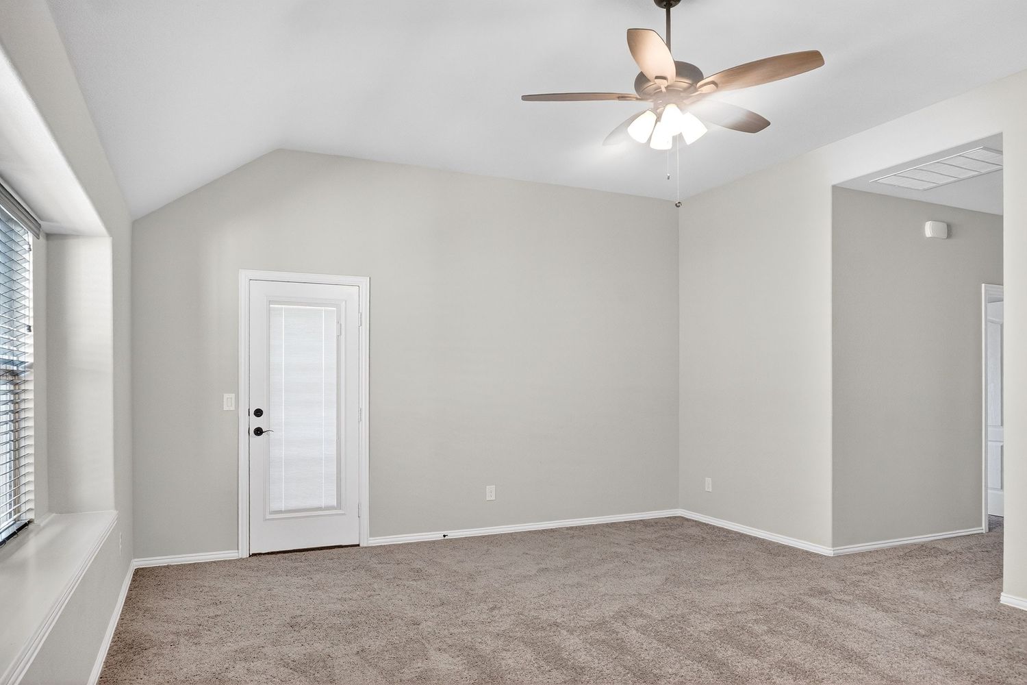 Large bedroom with vaulted ceiling, ceiling fan, and neutral gray carpeting.