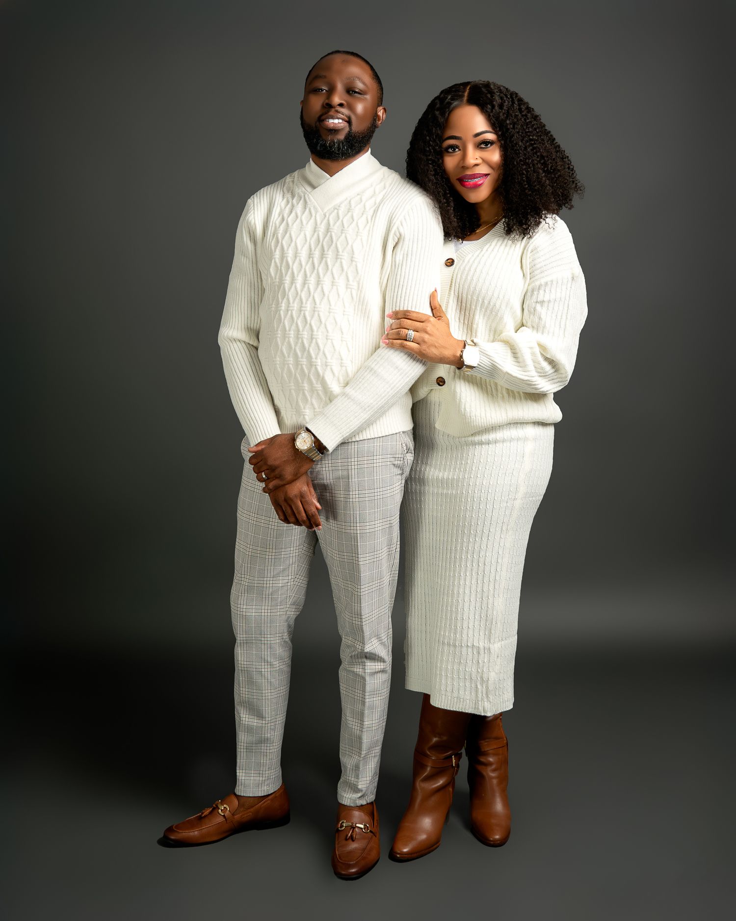 Couple in matching white sweaters pose for studio portrait against dark background.