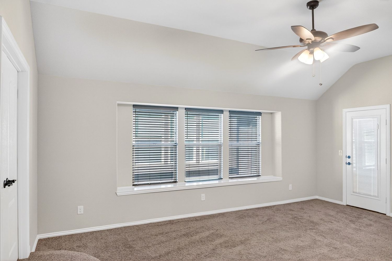Empty room with vaulted ceiling, ceiling fan, and large windows providing natural light.