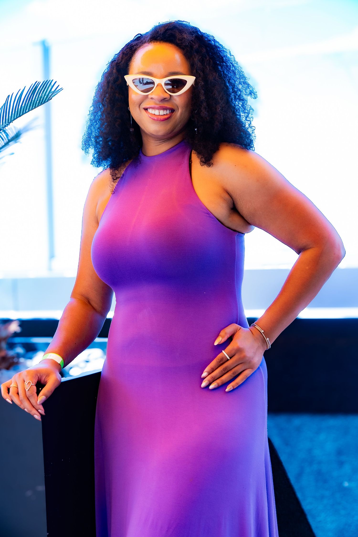 Confident poses in a bright purple ombre sleeveless dress against a blue backdrop.