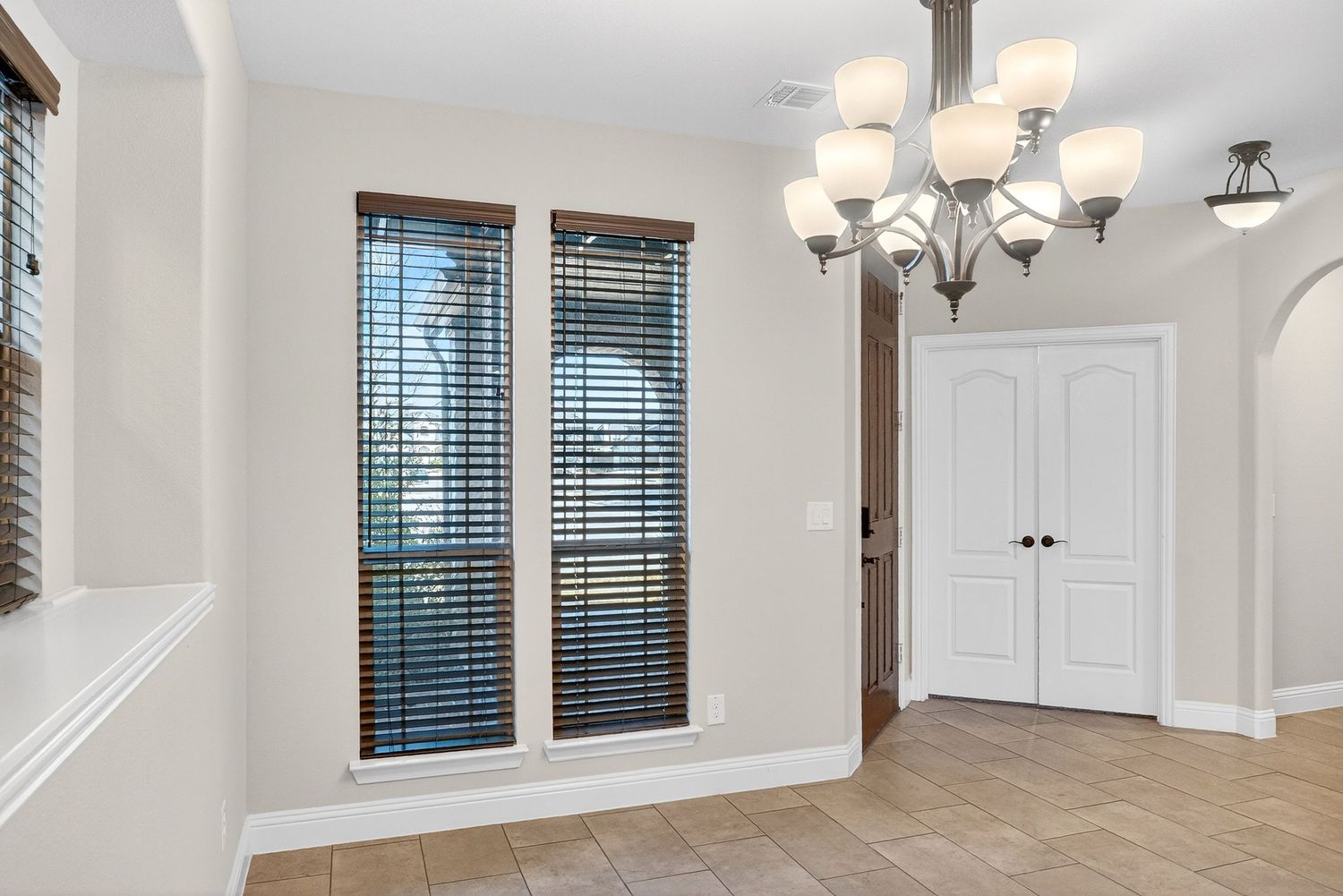 Spacious living area with vaulted ceilings, large windows, and elegant chandelier lighting.