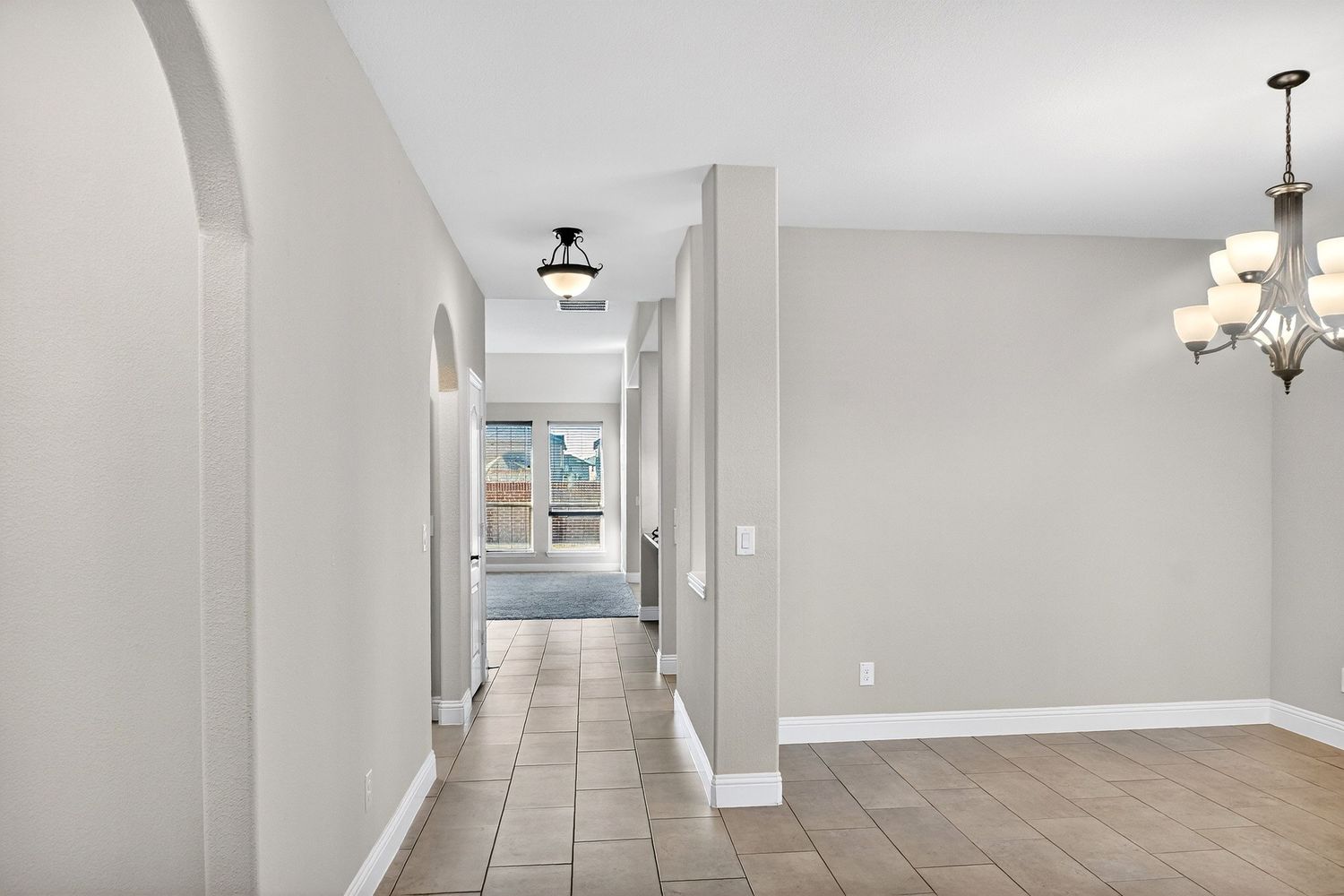 Long hallway with white walls, tile flooring and recessed lighting creates an inviting entrance space.