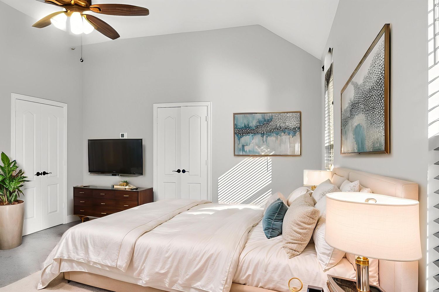 Cozy bedroom with ceiling fan, decorative artwork, and natural lighting from windows.