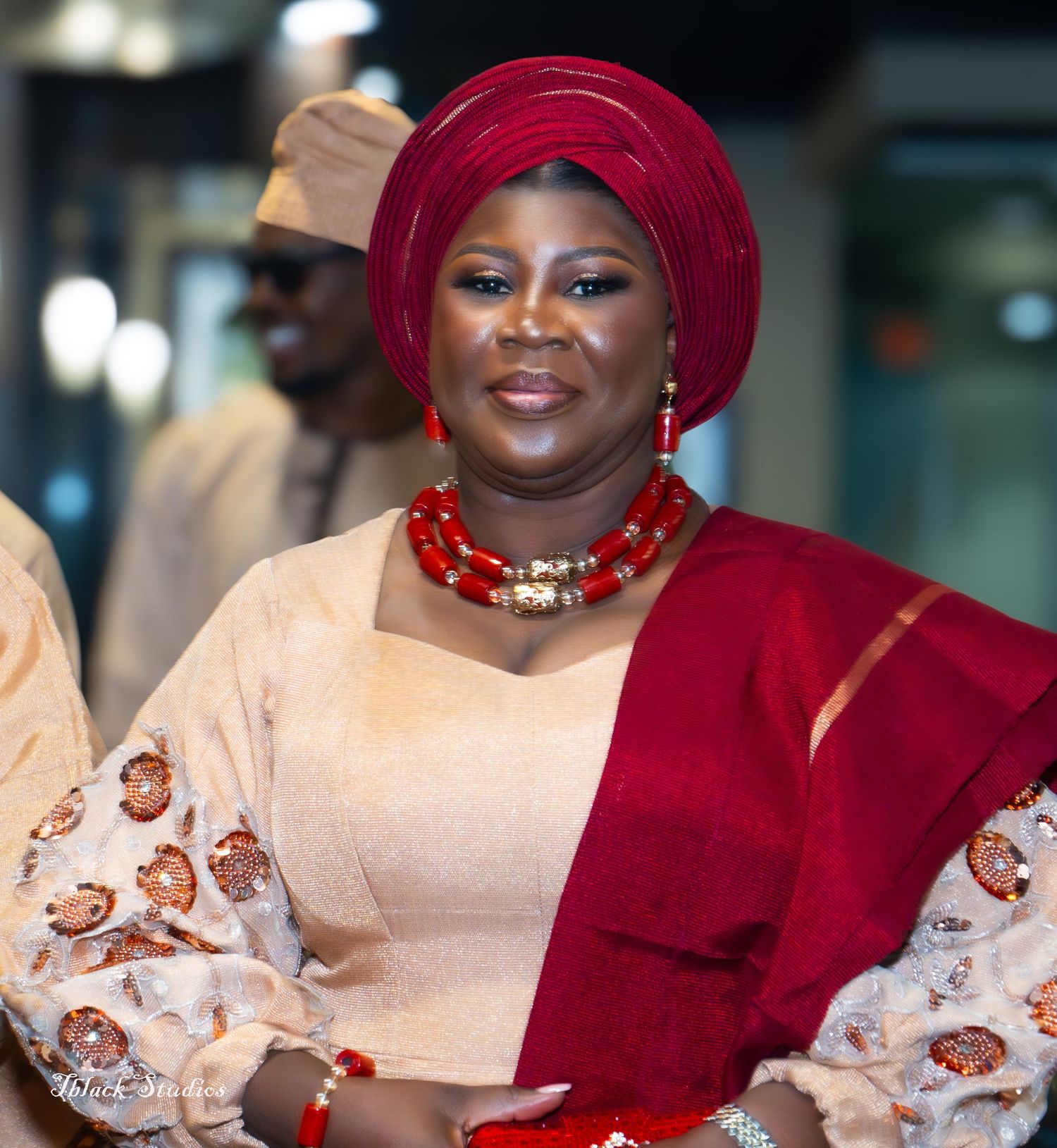 Elegant formal attire featuring a burgundy headwrap and cream colored dress with traditional Nigerian embellishments.