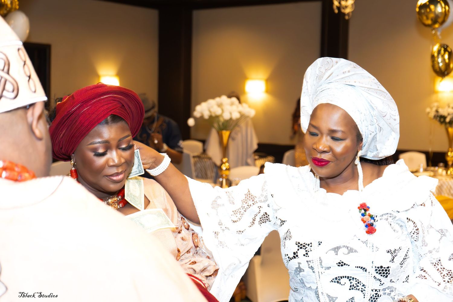 Traditional African wedding celebration with guests wearing white and red attire dancing together in a festive venue.