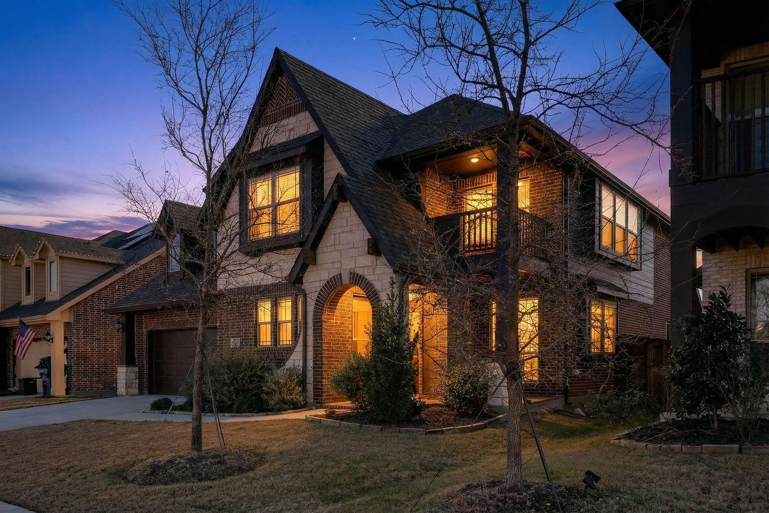 Row of luxury homes at dusk with warm glowing windows and dramatic twilight sky.