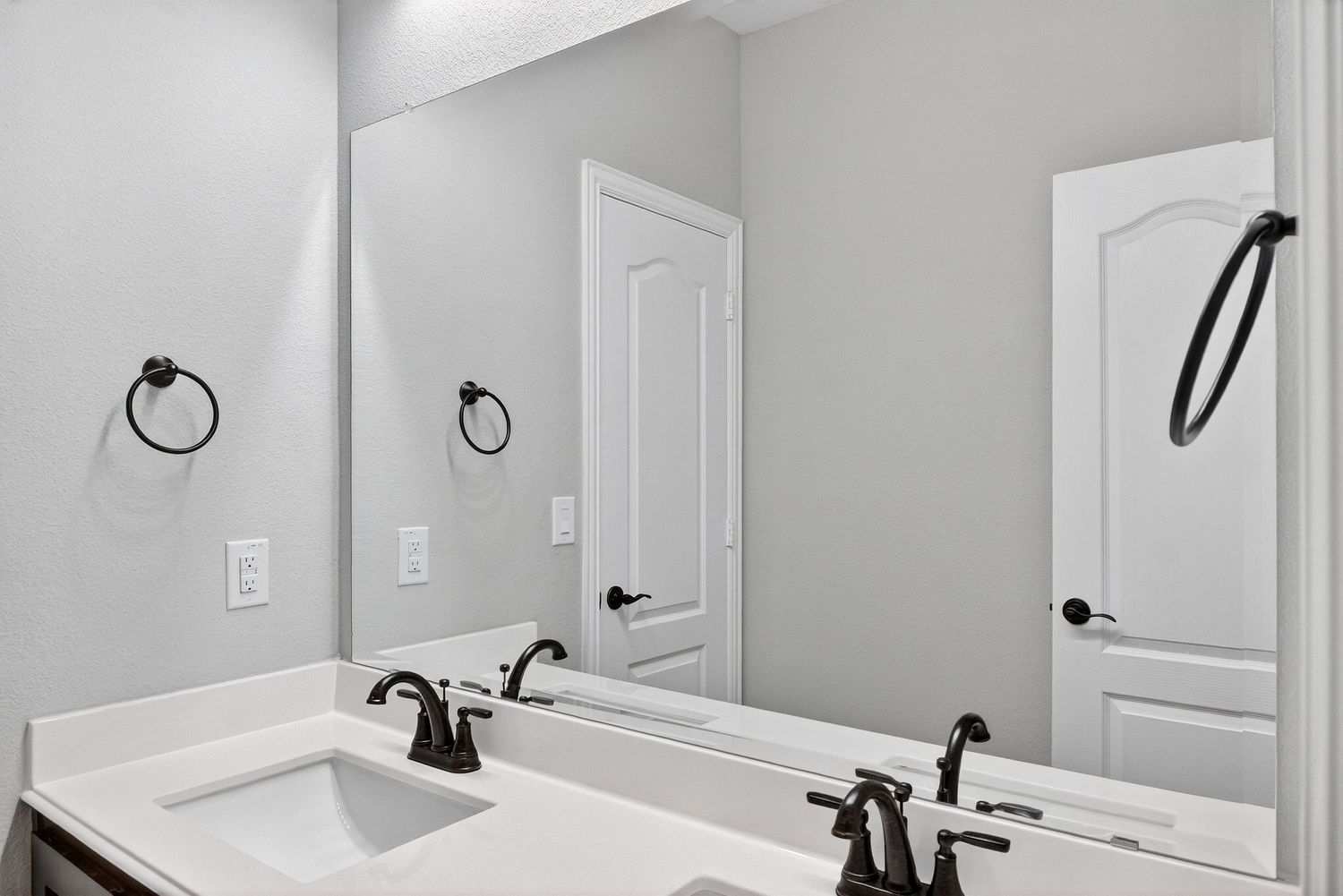 Modern bathroom with white vanity, dual sinks, and black faucets against light gray walls.