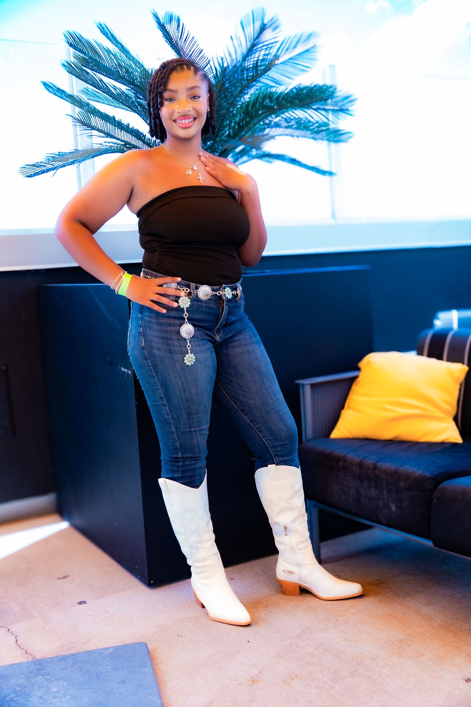 Person sitting on black couch wearing white boots and dark jeans with yellow pillow in background.