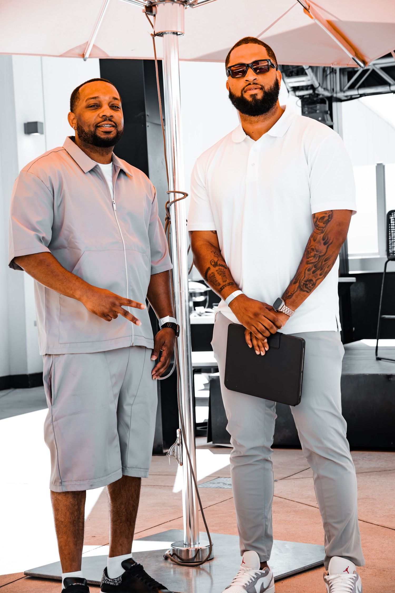 Two men in casual attire standing under white tent.