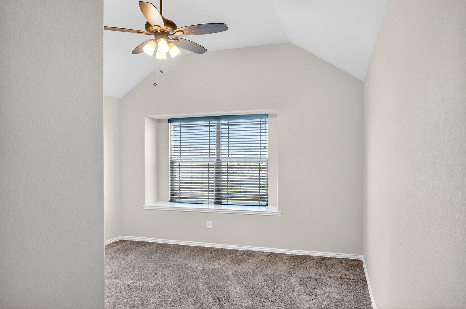 Empty room with vaulted ceiling, ceiling fan, and windows offering abundant natural light.