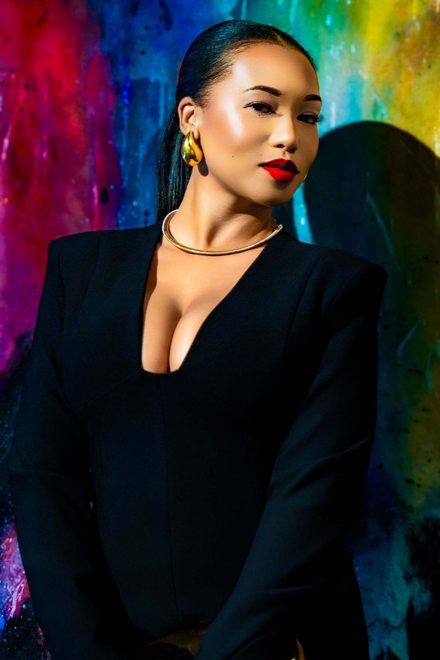 Artistic fashion shoot with black clothing against multicolored abstract wall.