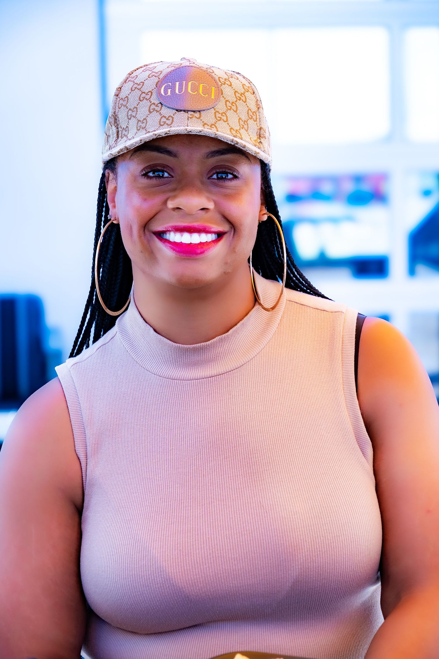 Woman in beige top and designer cap with large hoop earrings.