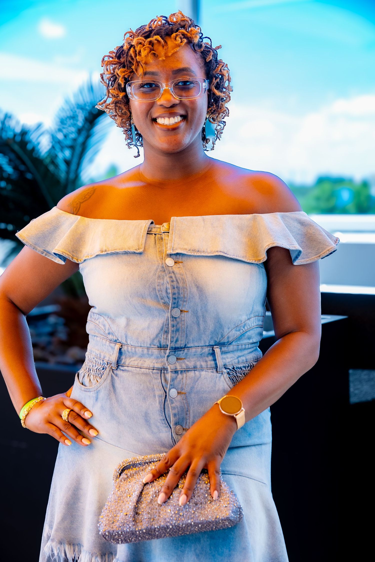 Person in light denim dress with ruffled neckline posing on outdoor terrace.