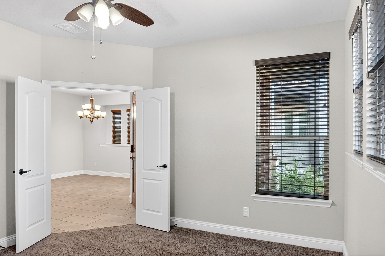 Ceiling fan with light fixture mounted in a bright white room with wood blinds and double doors.