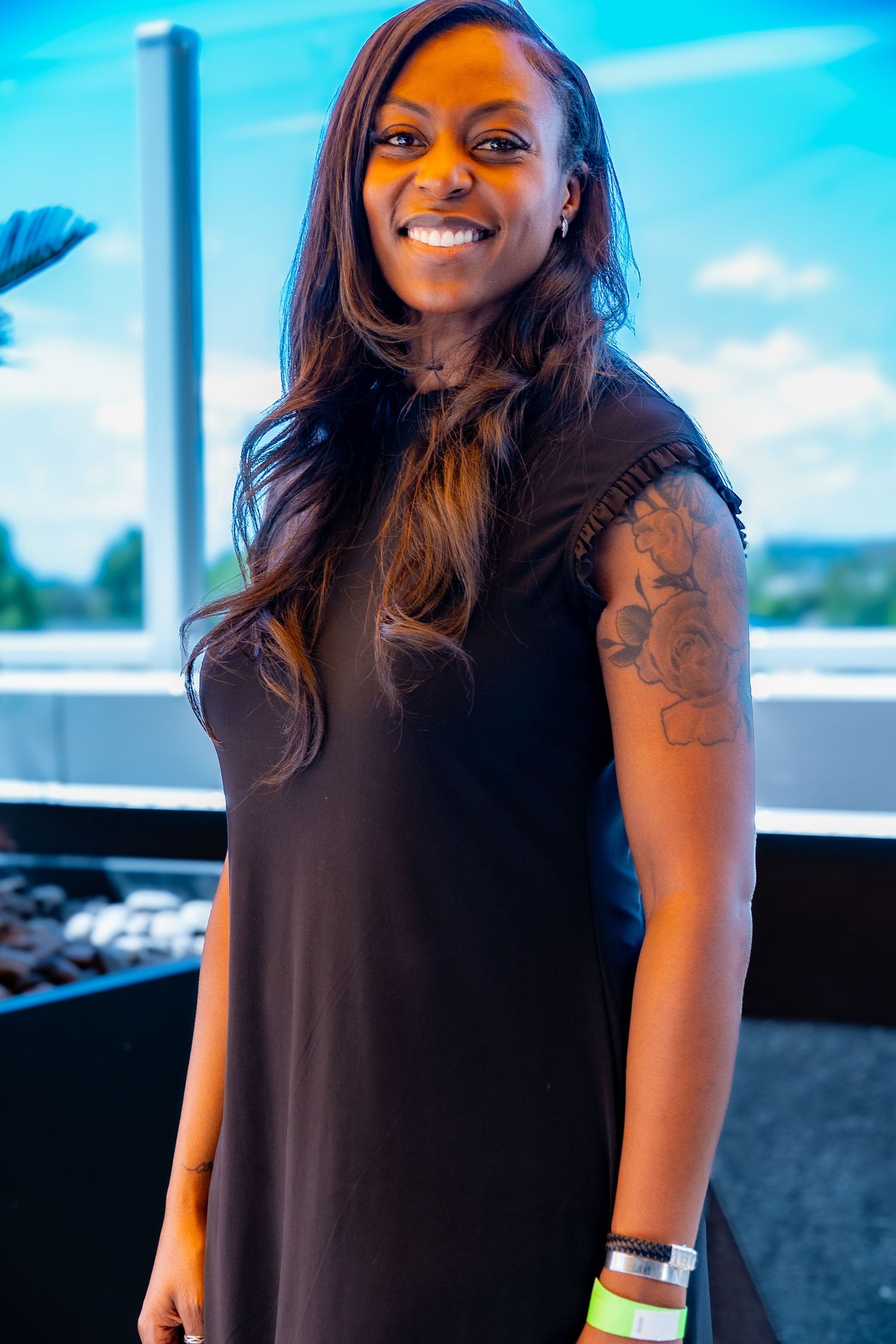 Person wearing black top with tattoo visible on arm posing near window.
