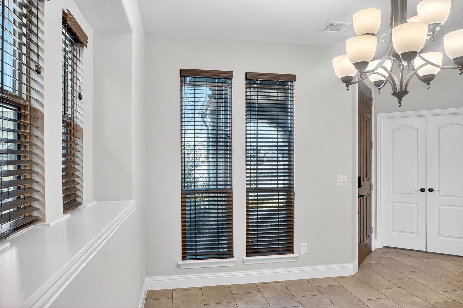 Modern hallway with white walls, dark wood blinds, and elegant pendant lighting fixtures.