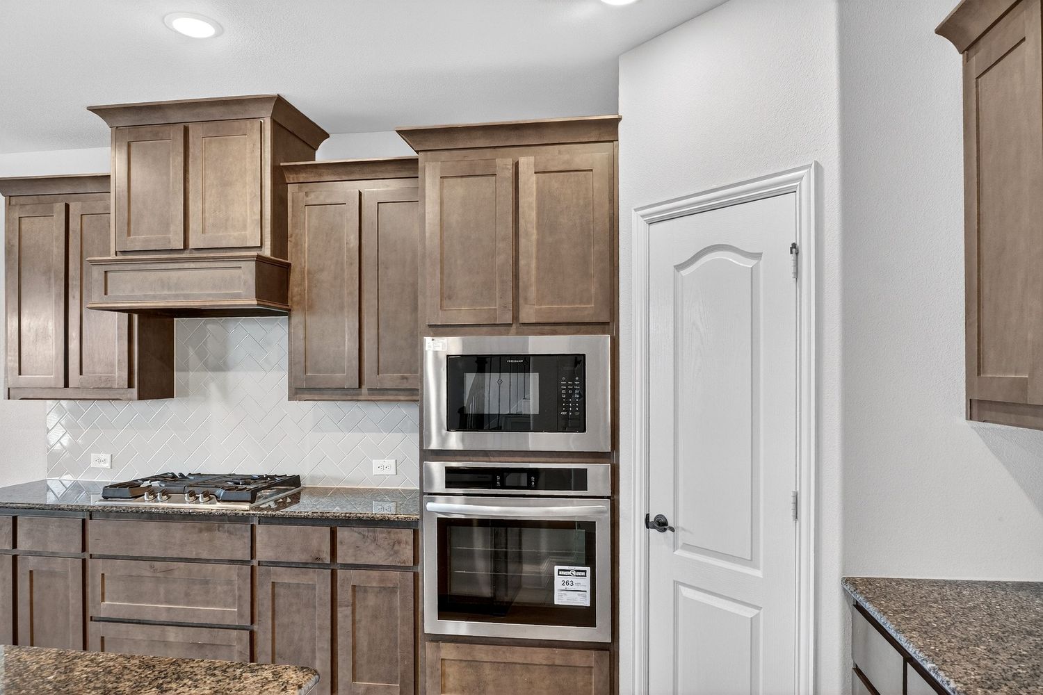 Modern kitchen with brown cabinetry, granite countertops, and stainless steel appliances.