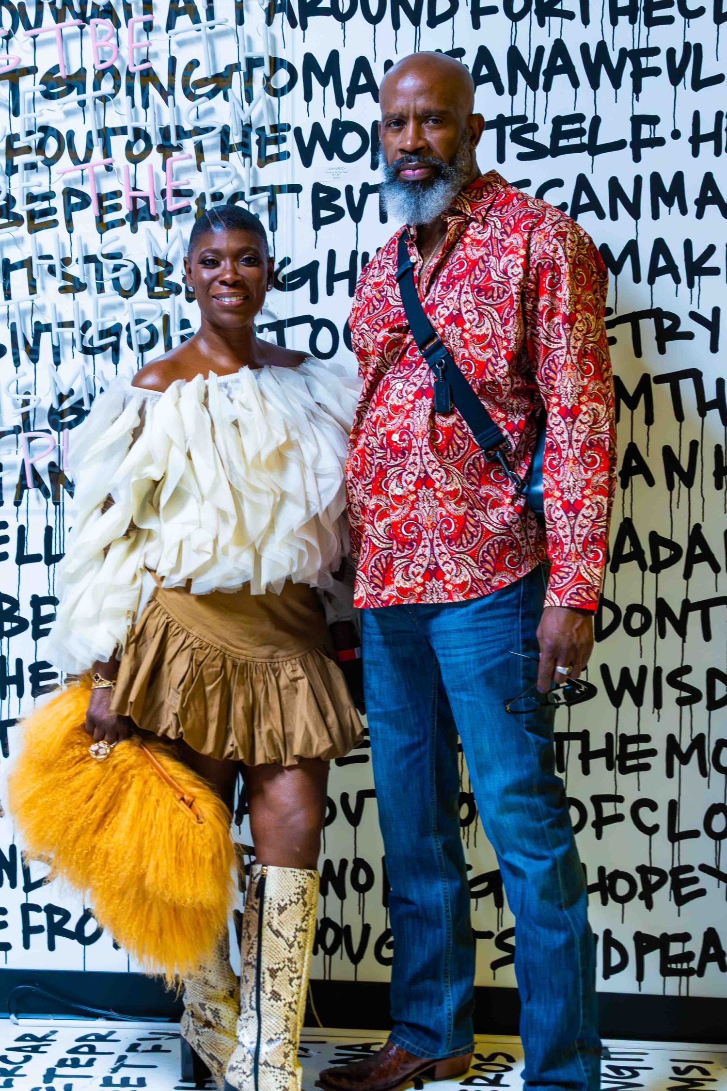 Performers in vibrant costumes pose against wall covered in black handwritten text.