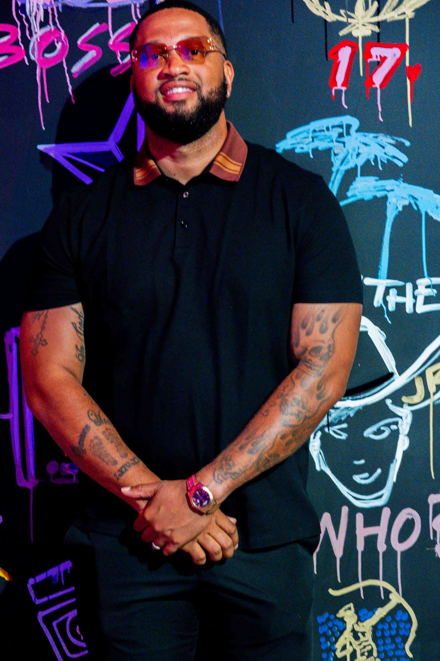 Person in black attire poses against graffiti wall with neon artwork.