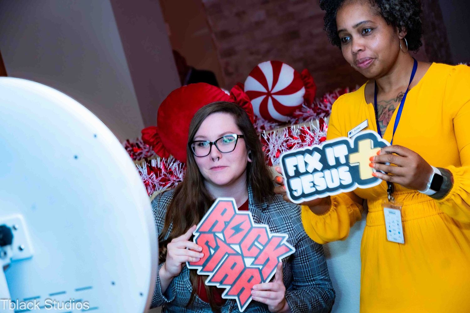 Two people holding decorative signs at a holiday party with peppermint candy decorations in the background.