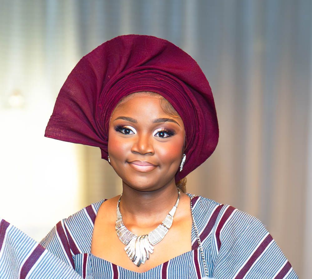 Close-up of attendant in burgundy headwrap and blue striped dress wearing white statement necklace.
