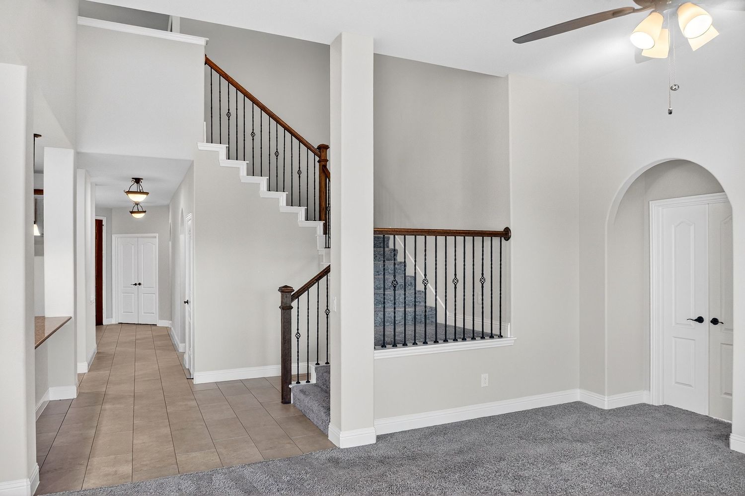 Long hallway with white walls, ceiling fan, and arched entryway leading to staircase.