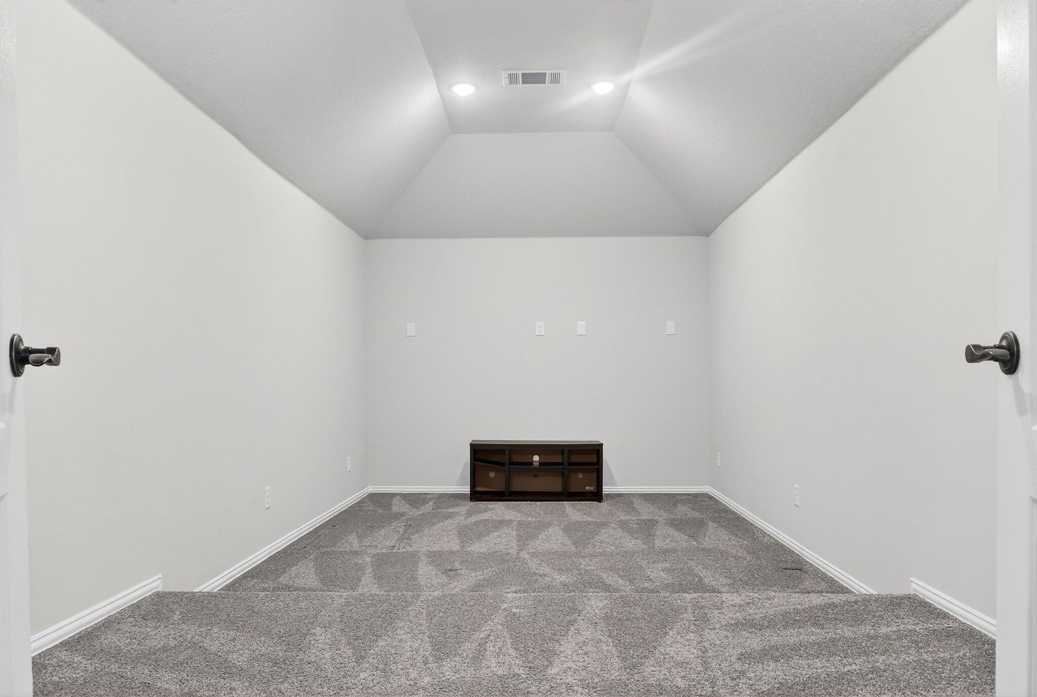 Long white hallway with recessed lighting and gray carpet leading to a bright room at the end.