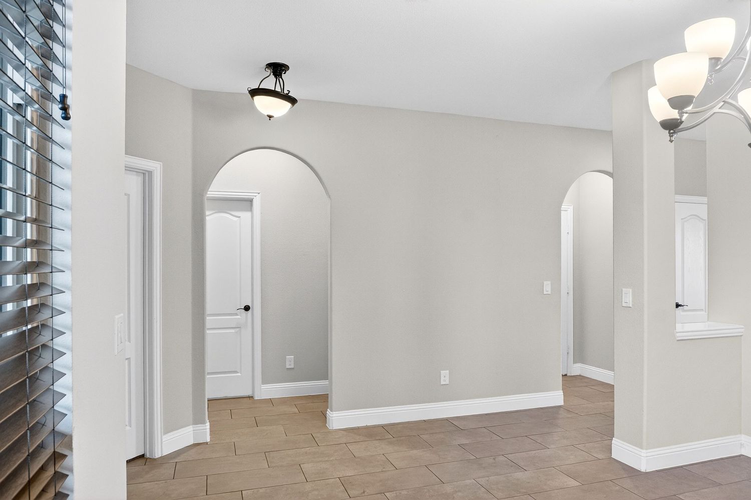 Modern interior hallway with arched doorways, beige tile floors and white trim details.