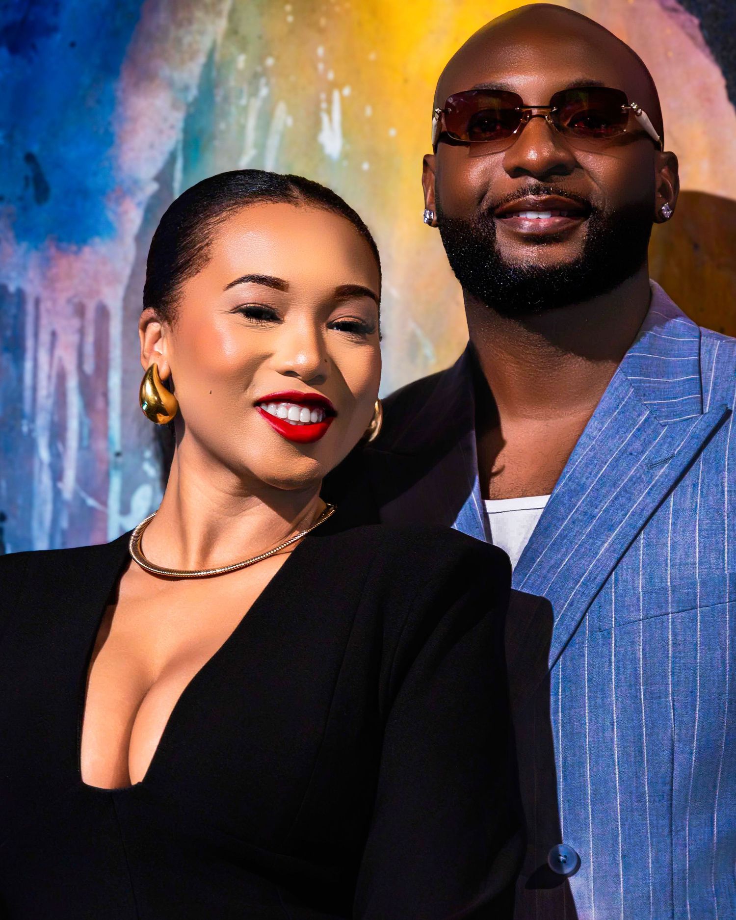 Glamorous couple poses against colorful abstract backdrop in formal evening wear.
