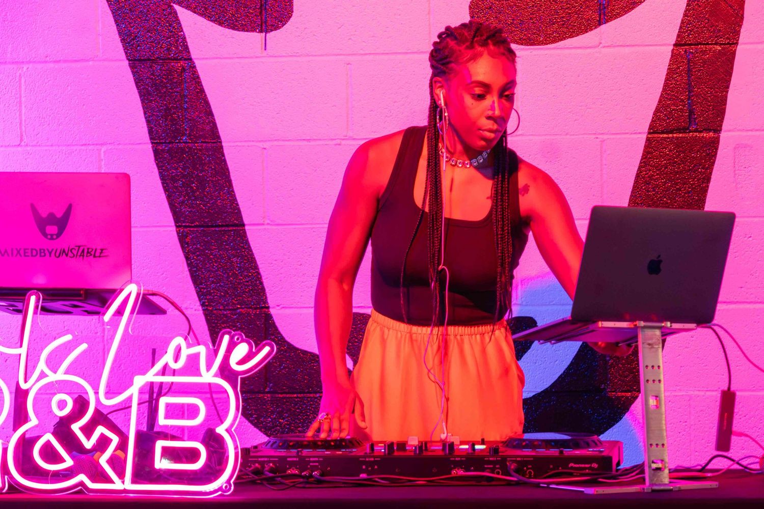 DJ performance scene with pink lighting and electronic equipment setup.