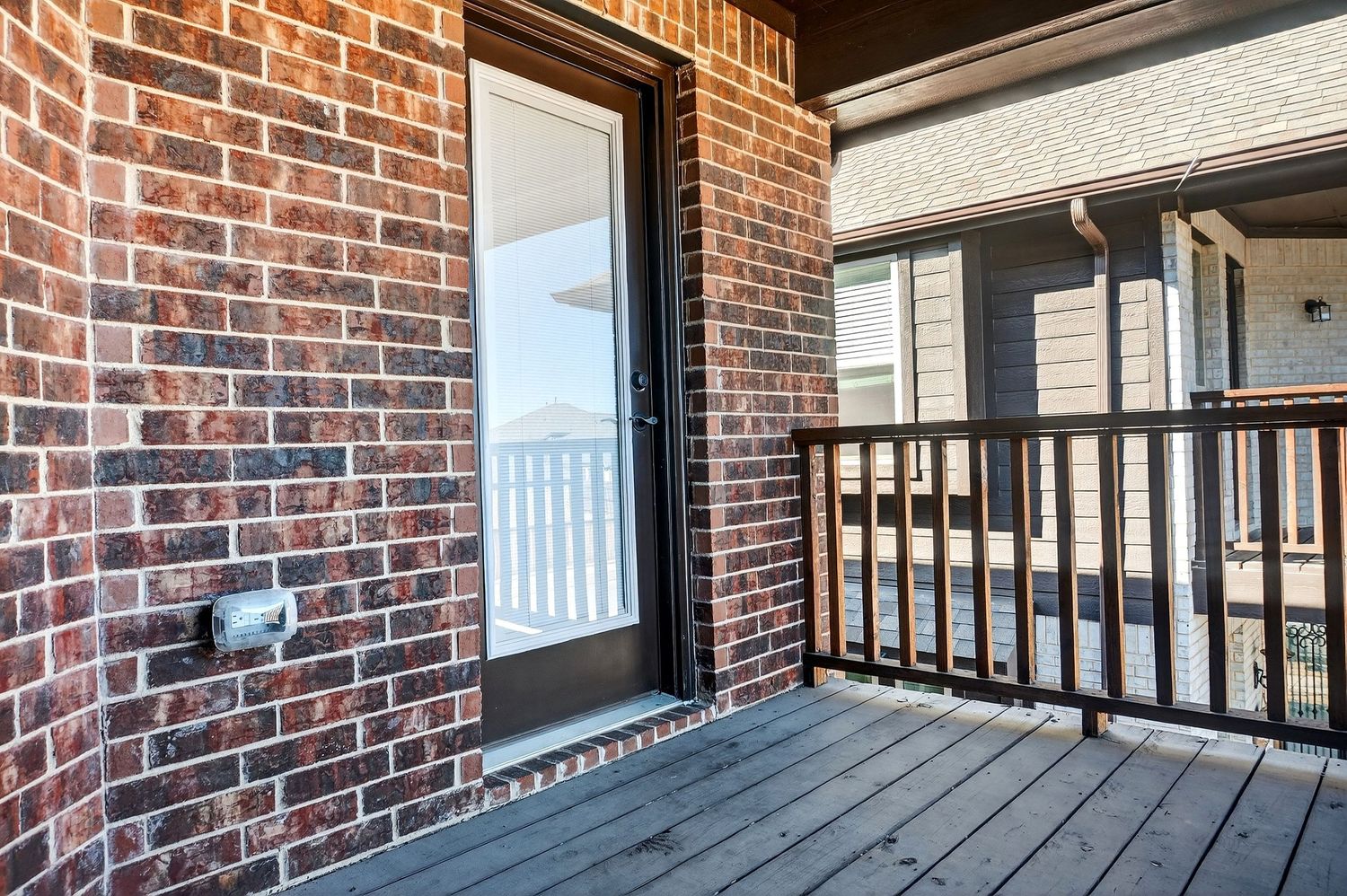 Brick exterior balcony with black metal railings and white trim details on a residential building.