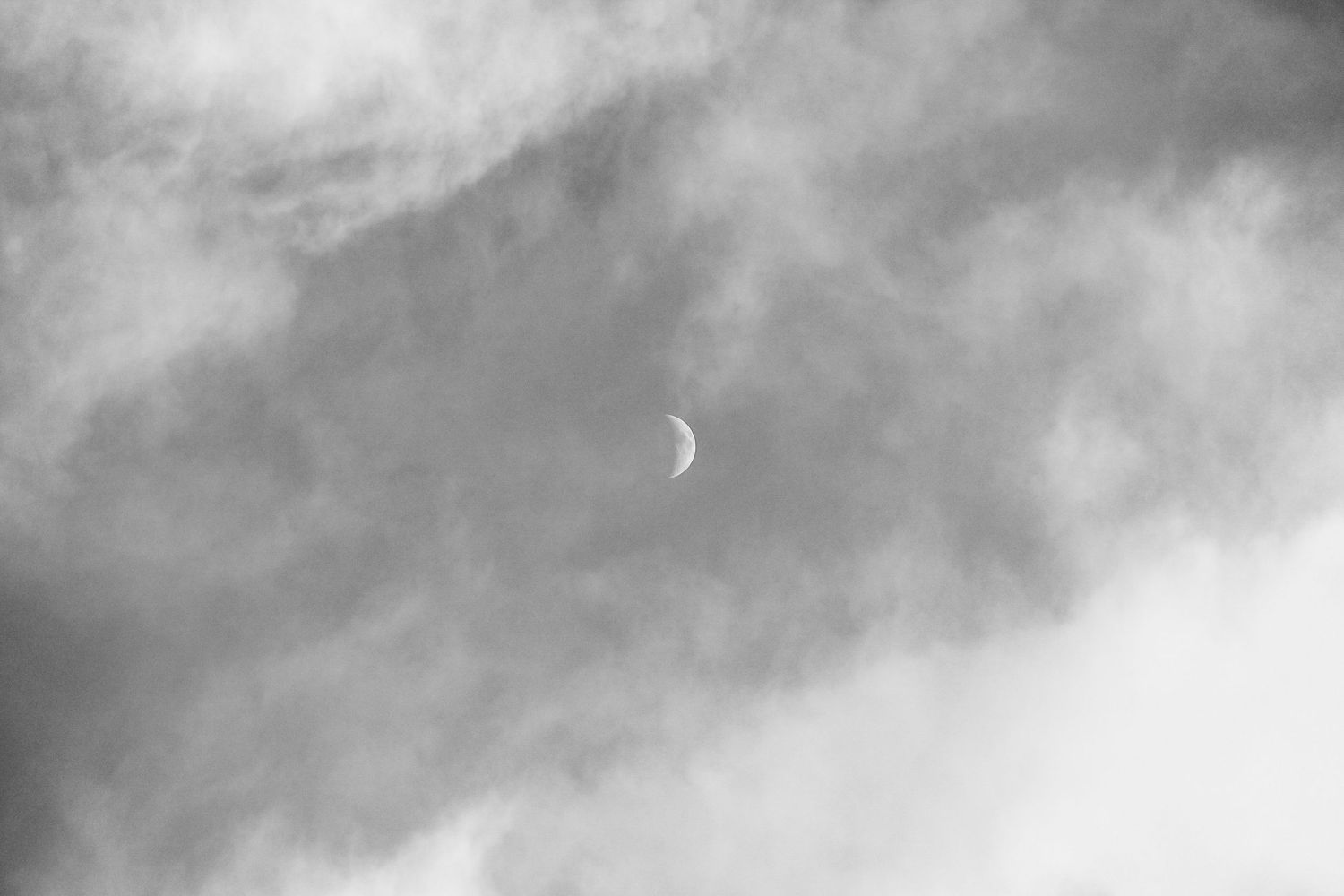 Half moon during a cloudy afternoon as black and white moon photography available as fine art prints and gallery frame.