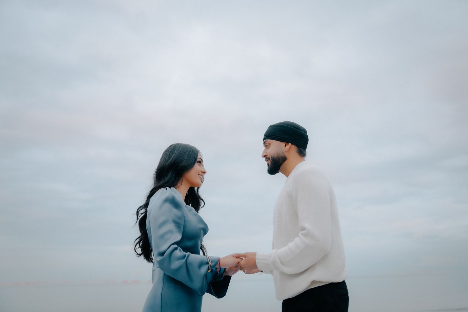 A couple holds hands while standing together against a cloudy sky backdrop.