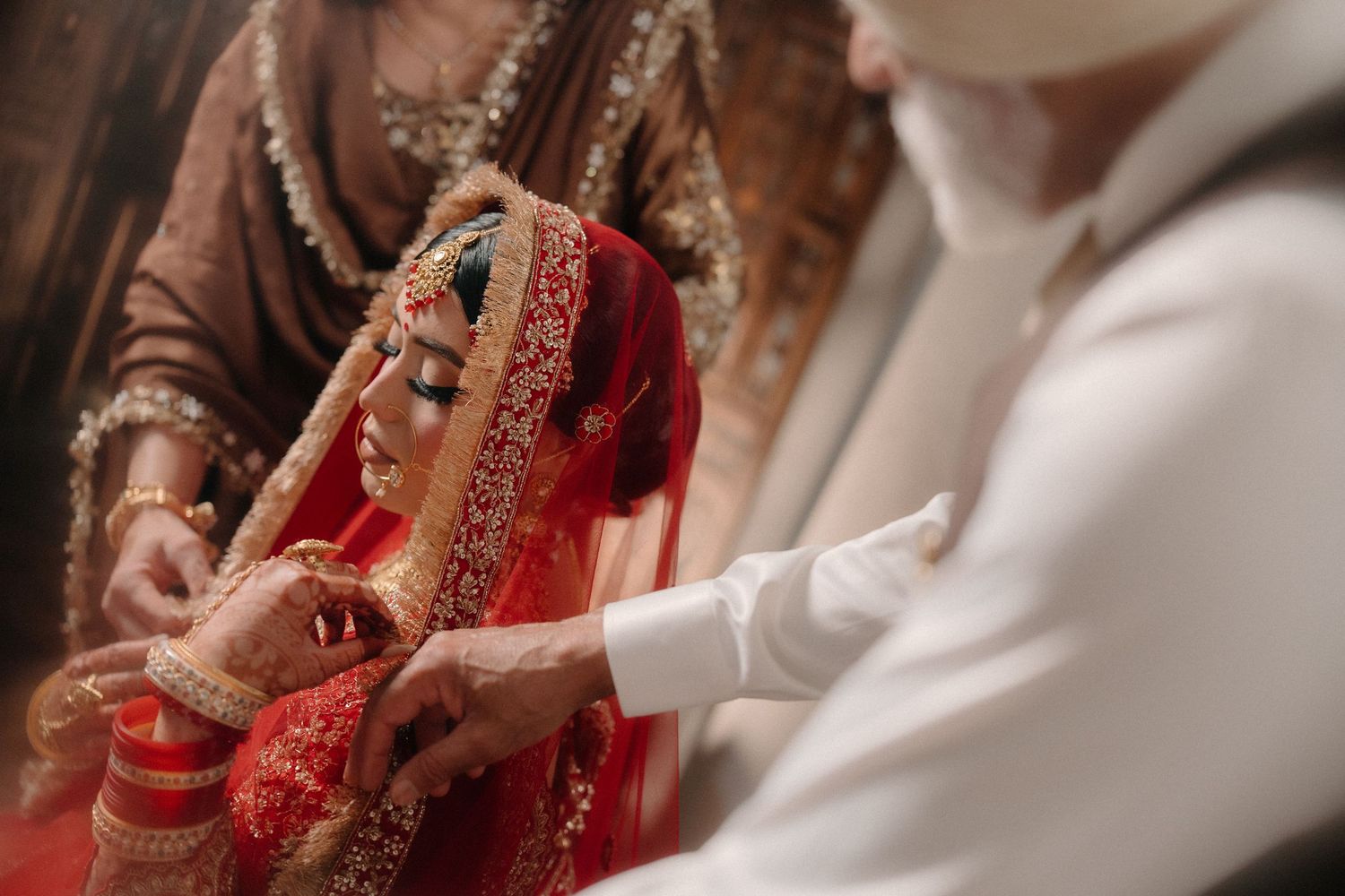 Traditional Indian wedding ceremony detail showing hands adjusting red and gold bridal attire and jewelry.