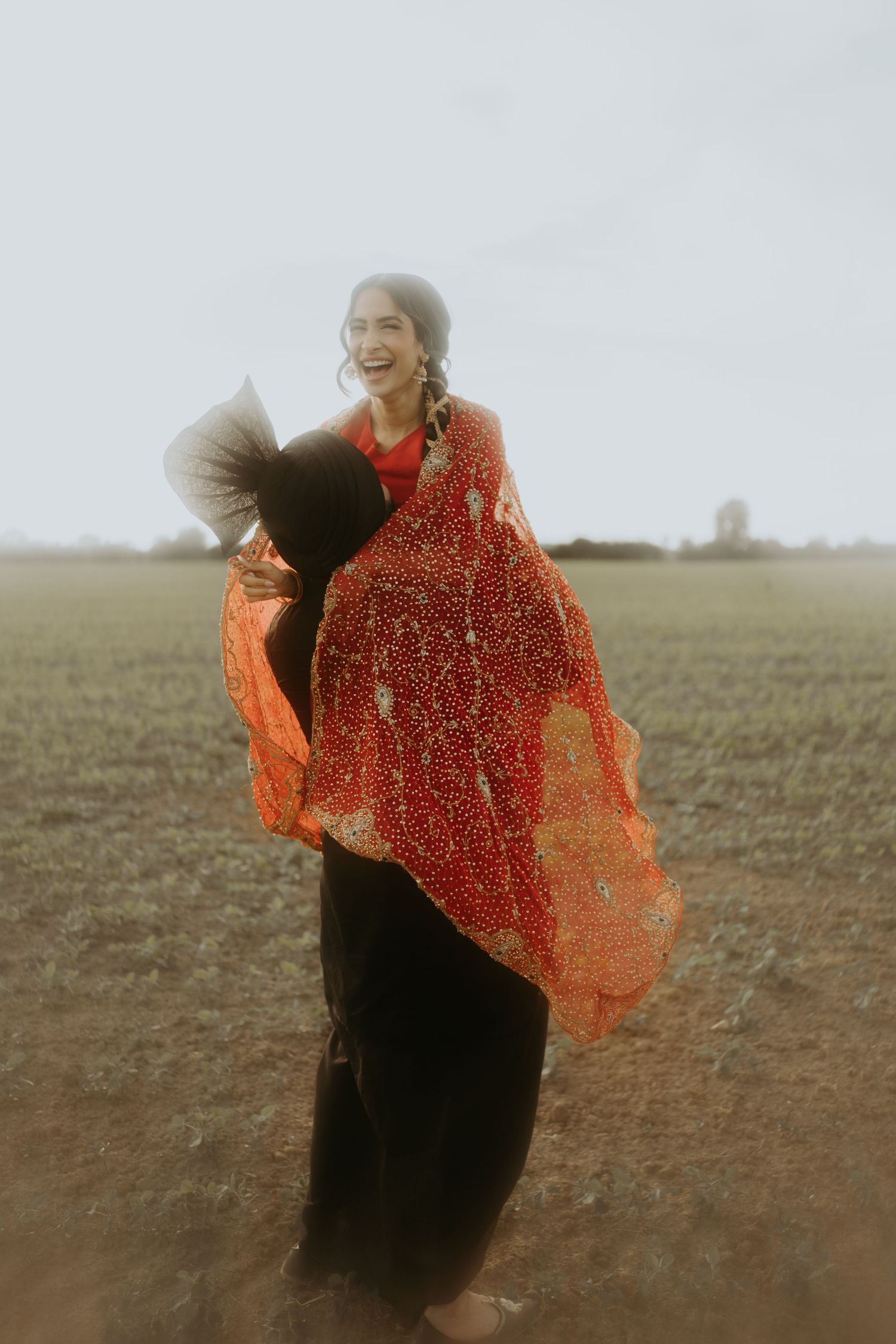 A person in a black dress dances in a field while holding a flowing red and orange sheer scarf in the wind.
